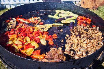 Various vegetables in a huge cauldron are cooked in oil.