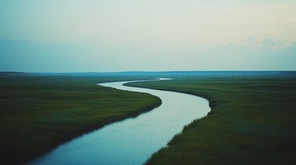 A tranquil river winds through expansive, lush green plains under a serene blue sky, embodying calmness and the beauty of unspoiled nature's wilderness.