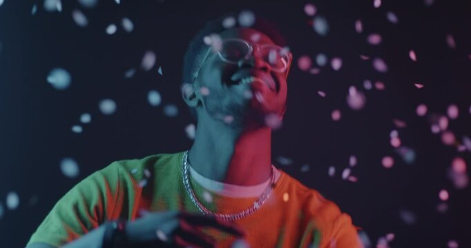 African American man dancing throwing confetti in neon light on dark background. Special occasion and entertainment concept.