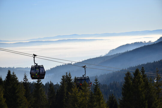 Cabin cable car ski lift glides above the mist-covered forest, breathtaking aerial view of the mountains and distant horizon. Layers of fog, valleys, high-altitude travel.  - Powered by Adobe