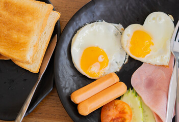 Top view shot of a delicious breakfast spread featuring heart shaped fried egg, ham, sausage and toast.