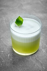 A refreshing green cocktail with a frothy top, garnished with a fresh basil leaf. The vibrant color...