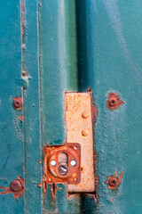 A close-up of an aged green metal door features a heavily rusted lock mechanism and corroded screws. The peeling paint and rust stains indicate years of exposure to the elements