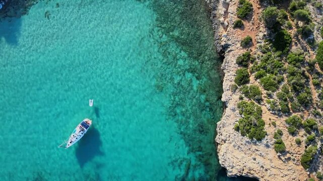 Experience the breathtaking beauty of Cala Varques with its crystal clear waters and rugged cliffs. Enjoy a tranquil day with boats gently gliding across the serene ocean, perfect for relaxation.