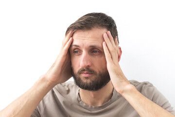 Fototapeta premium A bearded man in a beige t-shirt holds his head with both hands, looking tired and stressed, symbolizing headache, anxiety, and fatigue concept of health, stress,