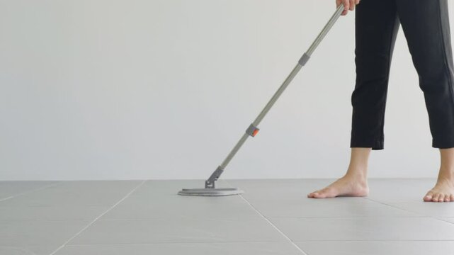 Woman mops the indoor floor, cleaning the front area of her home with a mop and rag. Housewife dedicated to maintaining cleanliness. Represents professional housekeeping and house maintenance concepts