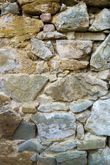 An old wall made of rough sandstone of different sizes. The connecting seams and deep cracks are visible. Some stones are covered with yellow moss.