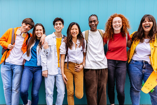 Portrait of seven young student friends leaning on blue wall. Youth and education concept
