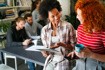 Diverse group of happy employees analyzing reports with digital device, working together in office