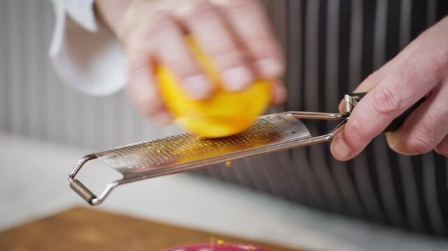 Food preparation. Professional chef grates orange peel with a metal grater. Slow motion 50 fps.