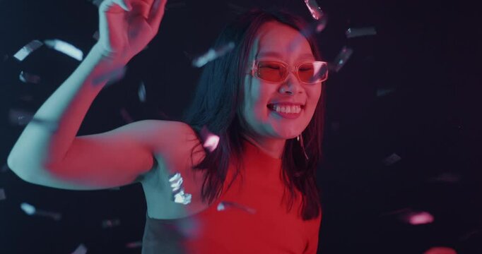 Slow motion of Asian girl dancing and catching confetti in neon light on dark background. Celebration and entertainment concept.