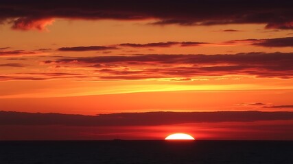 Obraz premium Fiery sunset over the ocean with a lone ship on the horizon, showcasing vibrant orange and red hues in the sky.