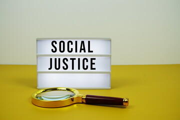 Social Justice text on LED lightbox with magnifying glass on yellow background