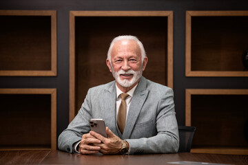 Portrait of successful and wealthy company director in business suit using smart phone in luxurious...