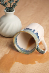 Coffee spills from cup on wooden surface with vase and flowers
