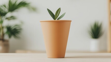A small green plant in an orange pot sits on a wooden surface, with soft, blurred background greenery, creating a fresh and serene atmosphere.