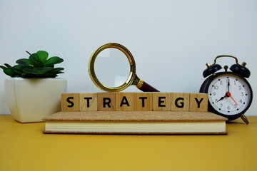 Magnifying glass and alarm clock with wooden blocks alphabet letters STRATEGY text message on...