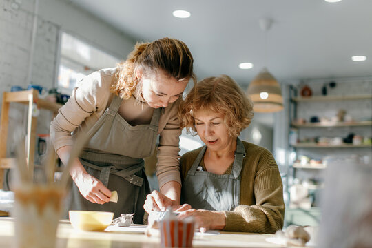 Elderly Caucasian woman learns pottery at a creative workshop with a young mentor. Two women work together with clay, developing skills and enjoying the artistic process