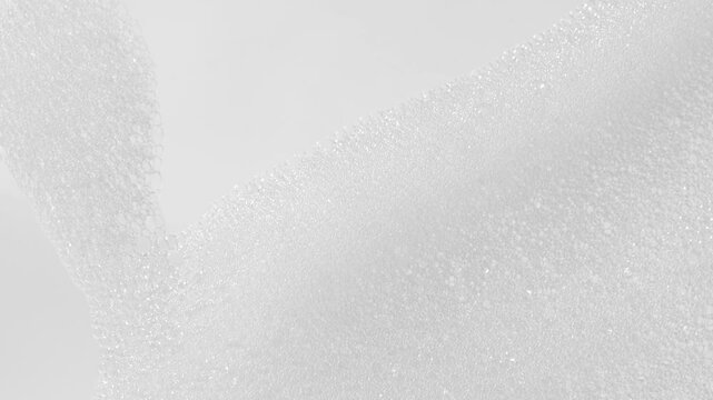 Fine bubbles of bath foam slide down the vertical glass surface, cosmetic texture.