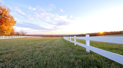 Fototapeta premium Autumn sunset over grassy field, white fence, idyllic rural scene, perfect for real estate