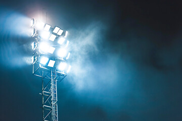 Intense stadium floodlights break through the dense fog, creating a dramatic and powerful scene.
