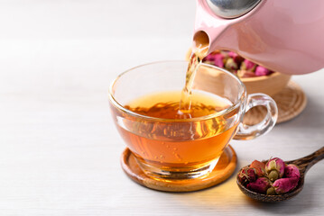 Rose tea in teapot pouring into cup glass on white background, Healthy flower tea