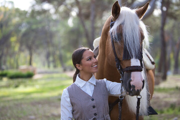 portrait of equestrian woman, young and beautiful, lovingly holding her purebred brown horse with blond mane by the head and joining her face together. The woman is happy. Love for the horse.