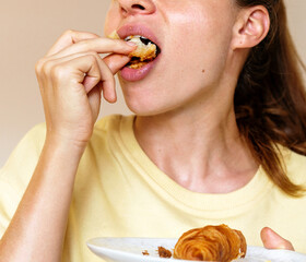 Overeating and Binge eating concept. Young hungry woman eating croissant 