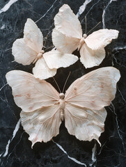 Three delicate, pale butterflies on dark marble.