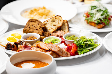 A hearty breakfast platter featuring eggs, sausages, fresh vegetables, and various dips. Rustic bread adds texture, and a vibrant array of colors makes it visually appealing. Perfect for food lovers.