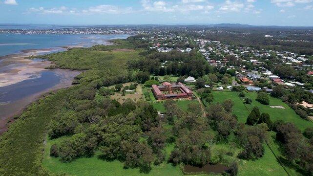 Aerial view of the beautiful Geoff Skinner Wetlands and coastal bay with urban area and historic Ormiston House, Brisbane, Australia.