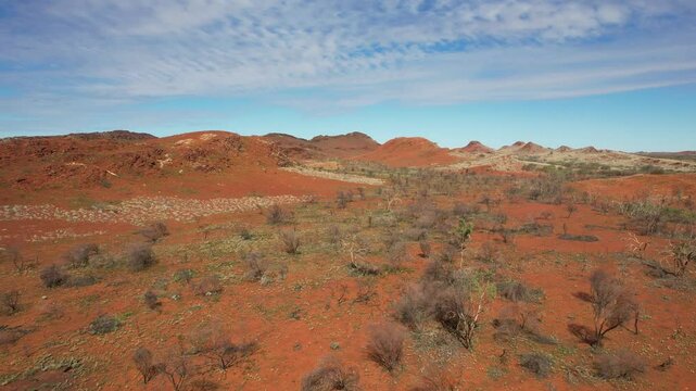 Aerial view of rugged red earth ridge and bushland under clear sky with clouds, Karratha, Western Australia.