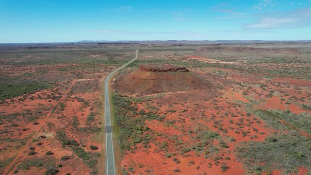 Aerial view of vast arid desert landscape with a scenic road and rugged plateau under a clear sky, N W Coastal Highway, Pilbara Region, Ashburton, Australia.
