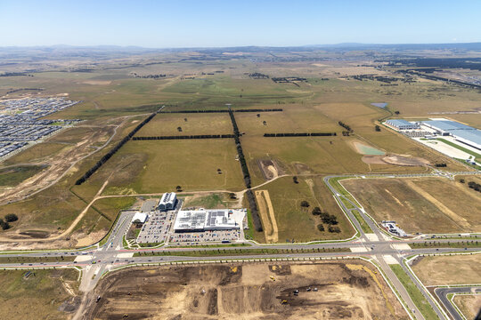 Aerial view of tranquil rural fields and modern suburban development with roads and buildings, Mickleham, Australia.