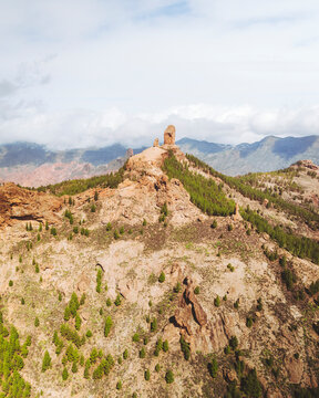 Aerial view of majestic Roque Nublo rock formation surrounded by serene forest and clouds, Tejeda, Spain.