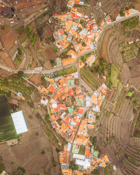 Aerial view of Agulo Stadium surrounded by picturesque terraced fields and traditional houses with orange roofs, Agulo, Spain.