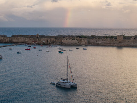 Aerial view of ancient castle ruins and serene sea with boats under a rainbow, Methoni, Greece.
