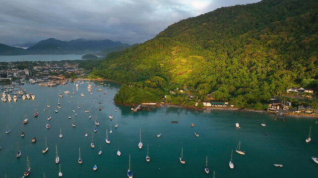 Aerial view of tropical archipelago with serene islands and boats in calm ocean under clouds at sunrise, Angra dos Reis, Brazil.