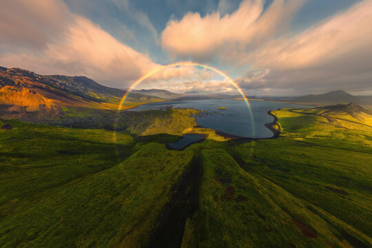 Aerial view of Frostastaoavatn lake with a vibrant rainbow amidst majestic mountains and lush greenery, Hella, Iceland.