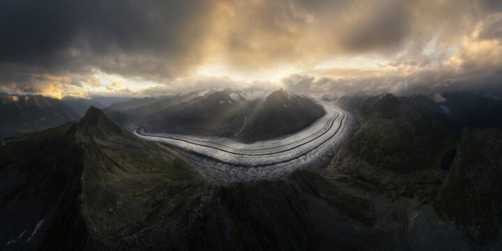 Aerial view of majestic Aletsch Glacier surrounded by rugged mountains under a dramatic sky, Fieschertal, Switzerland.