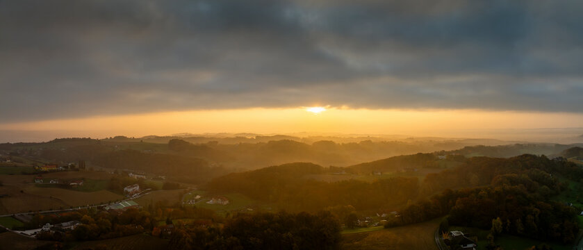Aerial view of serene sunrise over lush rolling hills and tranquil valley with misty clouds, Bad Loipersdorf, Austria.