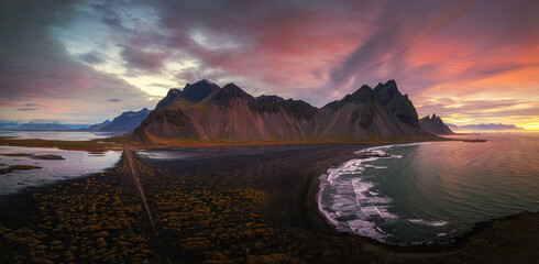Aerial view of dramatic sunset over rugged mountains and serene ocean along the picturesque coastline, Hofn, Iceland.