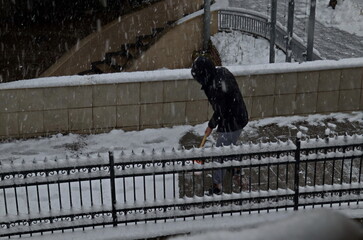 A young man carefully cleans the accumulated snow from a storm with strong winds and heavy snowfall in a residential area, Sofia, Bulgaria