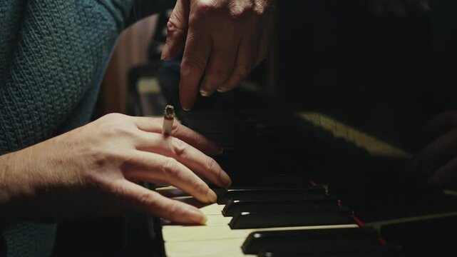 Pianist holds burning cigarette plays notes melancholy in sombre room. Close UP