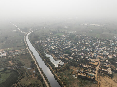 Aerial view of a beautiful rural village with homes, buildings, fields, and a canal, Gurki Mandi, Fatehpur Sikri, India.