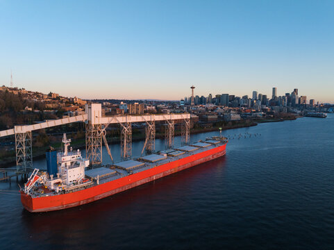 Aerial view of cargo ship and grain terminal with Seattle skyline at sunset, Elliot Bay, United States.