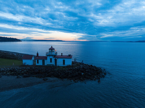 Aerial view of west point lighthouse at sunset over tranquil elliot bay and rocky coastline, seattle, united states.