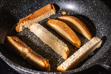 Slices of bread or croutons are toasted in a black pan