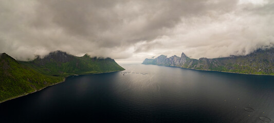 Aerial view of dramatic mountains and serene sea under cloudy skies, Senja Island, Lofoten, Norway.