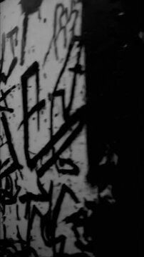 A grainy black-and-white image of an empty underground subway station, its walls covered in layered stickers and cryptic spray-painted messages.